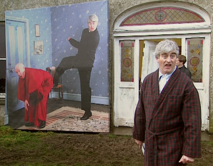 Ted standing next to a big picture of him kicking Bishop Brennan up the arse, on location