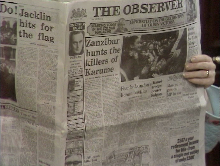 A paper being held by Joan - The Observer. Main headline: Zanzibar hunts the killers of Karume