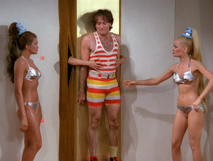 Robin Williams against the wall, two hands sticking out beside him
